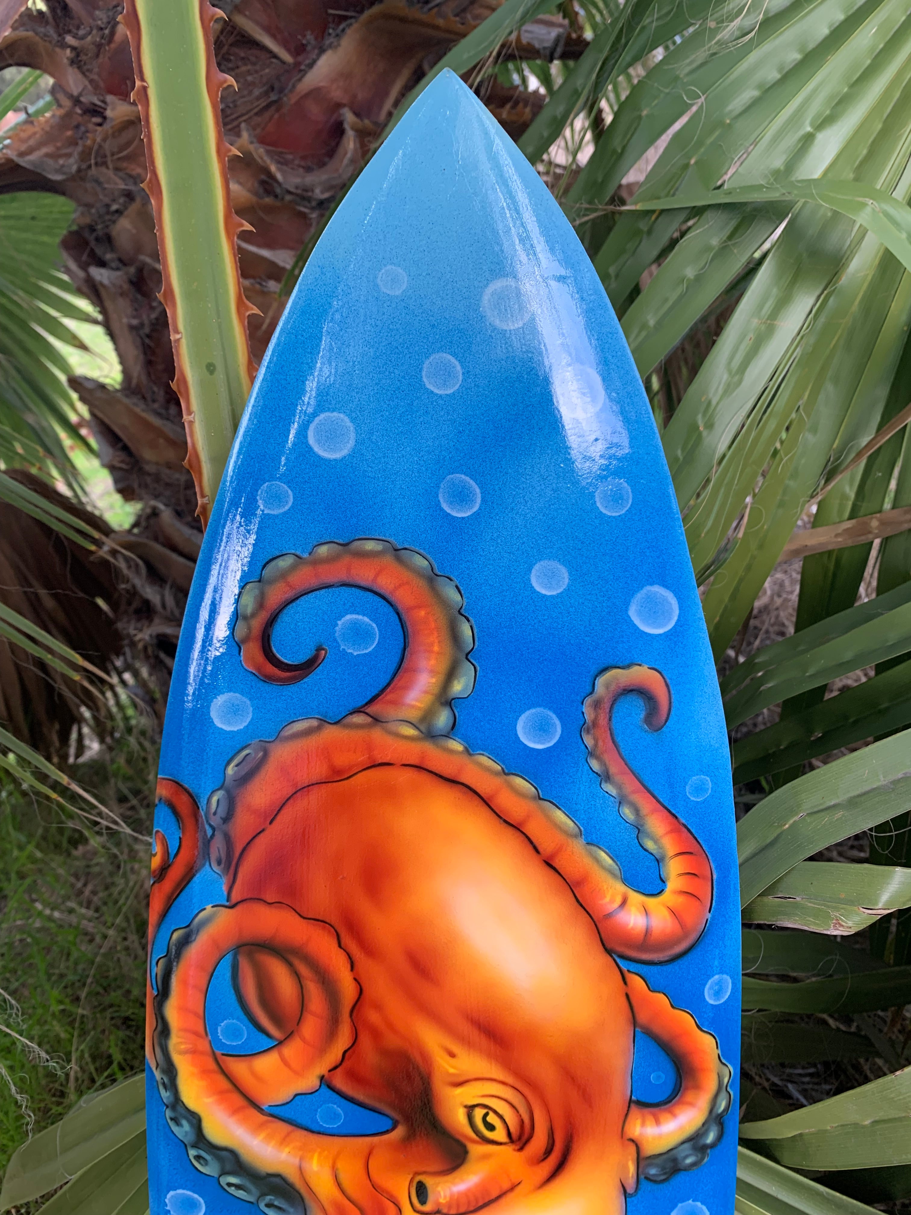 Blue surfboard featuring an orange octopus illustration with circular bubbles.